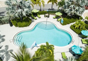Vista aérea de una piscina rodeada de palmeras y sillones de jardín verdes.