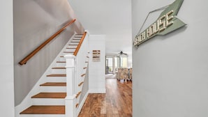 Un escalier avec des marches en bois et des rampes blanches mène à un espace de vie doté d’un plancher en bois et d’une enseigne fixée au mur.