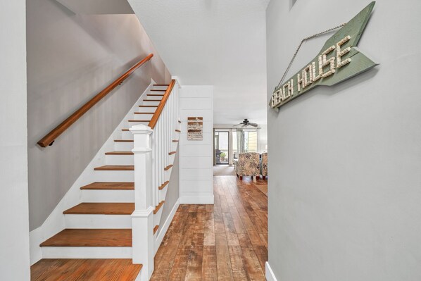 A staircase with wooden steps and white railings leading to a living area with a wooden floor and a wall-mounted sign.