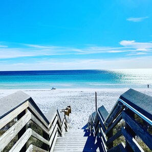 A wooden boardwalk leading to a beach with clear blue water and a bright sky.