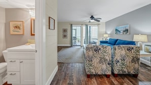 Un salon spacieux avec un grand canapé bleu, un ventilateur de plafond et une vue sur l’extérieur.