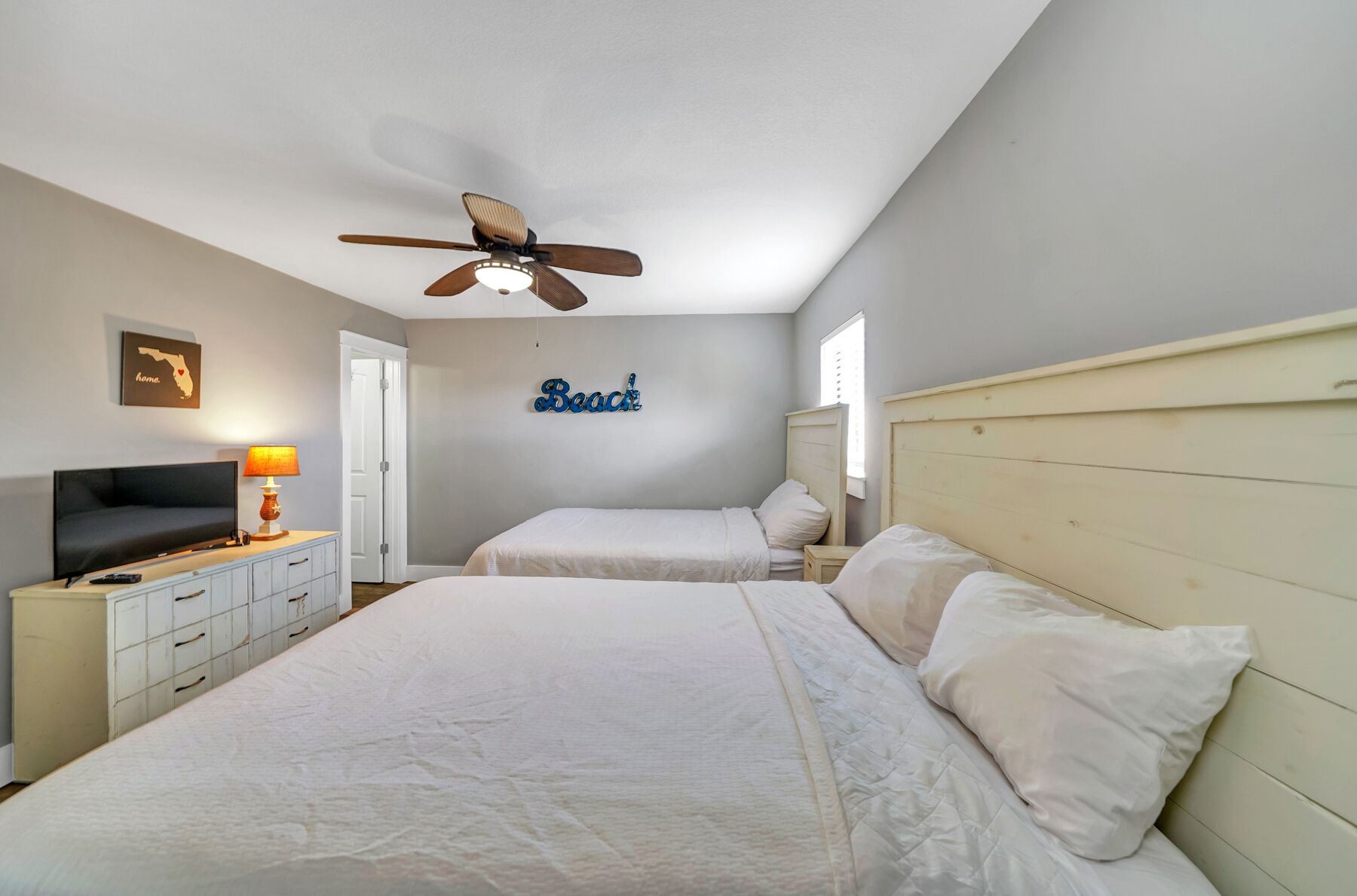 Une chambre d’hôtel avec deux lits, un ventilateur de plafond, une télévision et une lampe.