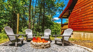 A wooden cabin with a stone fire pit surrounded by Adirondack chairs.
