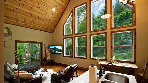 A spacious living area with a large window overlooking a forest, a cozy seating area, and a kitchen with a sink and countertop.