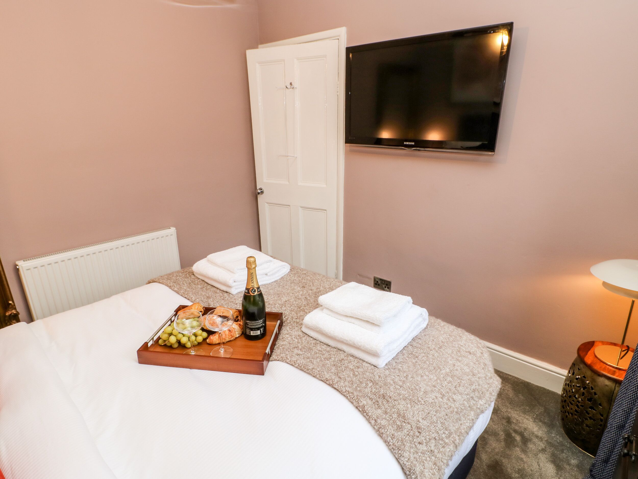 A hotel room with a bed, a tray with food and drinks, a TV on the wall, and a door.