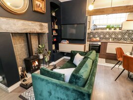 Una sala de estar moderna con chimenea, sofá verde y televisor montado en la pared.