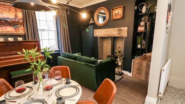 A dining area with a round table set for two, a green sofa, and a piano in the background. - Jaipur House (Richmond)