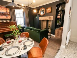 Un área de comedor con una mesa redonda preparada para dos personas, un sofá verde y un piano al fondo.