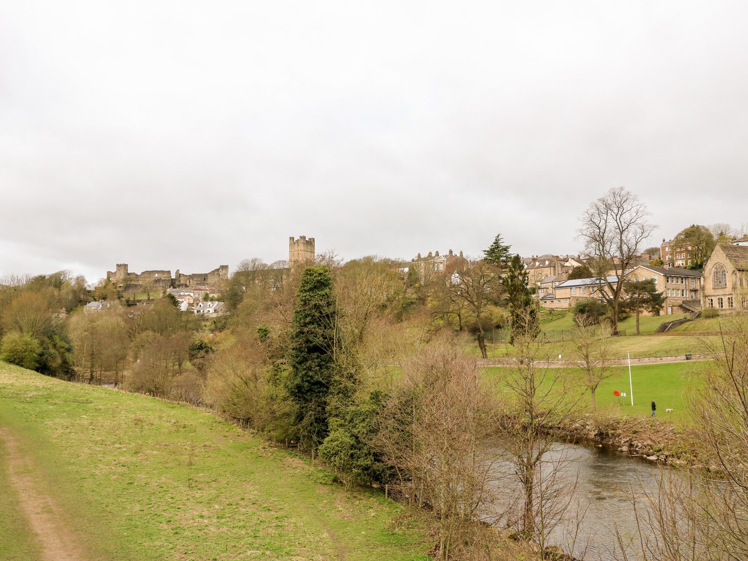 A castle on a hill with a river in the foreground and houses in the background.