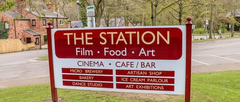 Letrero de 'The Station' que anuncia servicios como cine, cafetería/bar, microcervecería, panadería, estudio de baile, tienda de artesanías, heladería y exposiciones de arte.