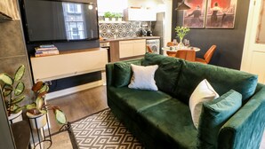A modern living room with a green sofa, a flat-screen TV, and a kitchen in the background. - Jaipur House (Richmond)