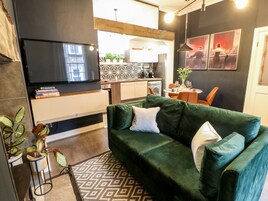 Una sala moderna con un sofá verde, un televisor de pantalla plana y una cocina al fondo.