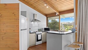 Une cuisine moderne dotée d’un îlot central, de meubles blancs, d’une cuisinière, d’un four et d’un four à micro-ondes. Une grande fenêtre offre une vue sur l’extérieur.