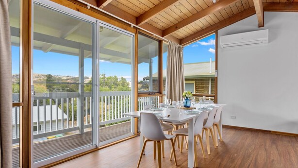 Un espace repas avec une table dressée pour six personnes, de grandes portes-fenêtres coulissantes et une vue sur l’extérieur.