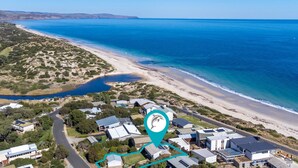 Vue aérienne d’une zone côtière comprenant une plage, un petit lac et un ensemble de maisons équipées de panneaux solaires.