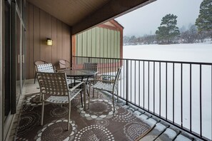 A covered outdoor area with a glass table and metal chairs, a patterned rug, and a view of a snowy landscape.