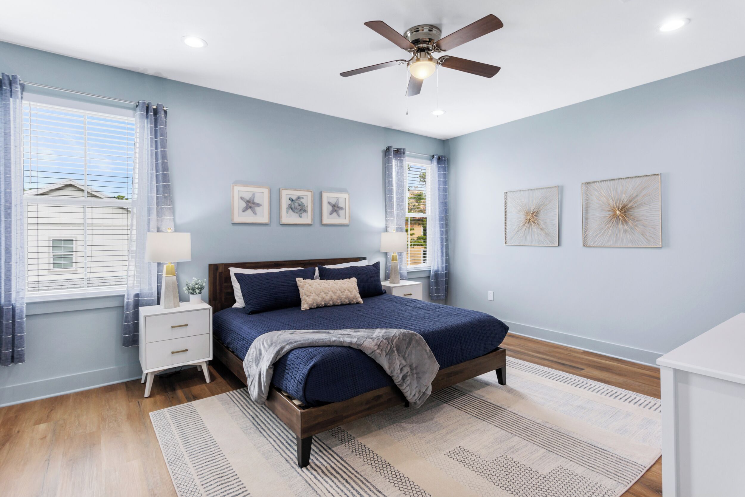 A bedroom with a bed, nightstands, a ceiling fan, and artwork on the walls.