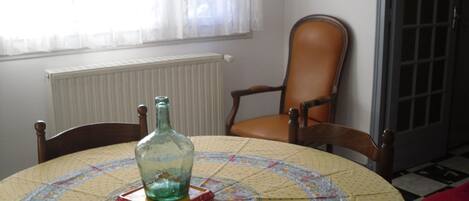 A round table with a floral tablecloth, a glass bottle, and a chair with a leather seat.