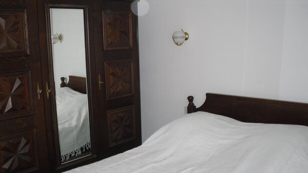 A bedroom with a wooden wardrobe, a bed with white bedding, and a wall-mounted light fixture. - Village house near spain, sea, lake, shops nearby (Le Boulou)