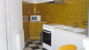 A compact kitchen with yellow tiles, a microwave, a stove, and a sink. - Village house near spain, sea, lake, shops nearby (Le Boulou)
