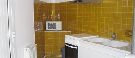 A compact kitchen with yellow tiles, a microwave, a stove, and a sink.