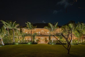 A large, well-lit building with a symmetrical facade, surrounded by palm trees and a well-maintained lawn.