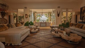 Un salon spacieux avec un grand canapé, une table basse et des objets décoratifs. On peut apercevoir un jardin à travers une porte ouverte.