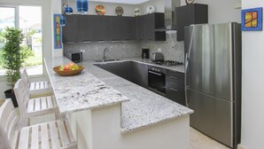 Une cuisine moderne dotée de plans de travail en granit, d’appareils électroménagers en acier inoxydable et d’un îlot central.
