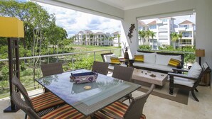 Un balcon doté de meubles en osier, d’une table en verre et offrant une vue sur un quartier résidentiel.