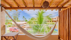 A hammock on a balcony with a view of palm trees and a red van in the background. - IT28 Triplex 4 Suítes 100m da Praia (Camaçari)