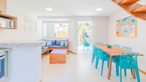 A bright kitchen with a wooden bench, a dining area with turquoise chairs, and a large window. - IT28 Triplex 4 Suítes 100m da Praia (Camaçari)