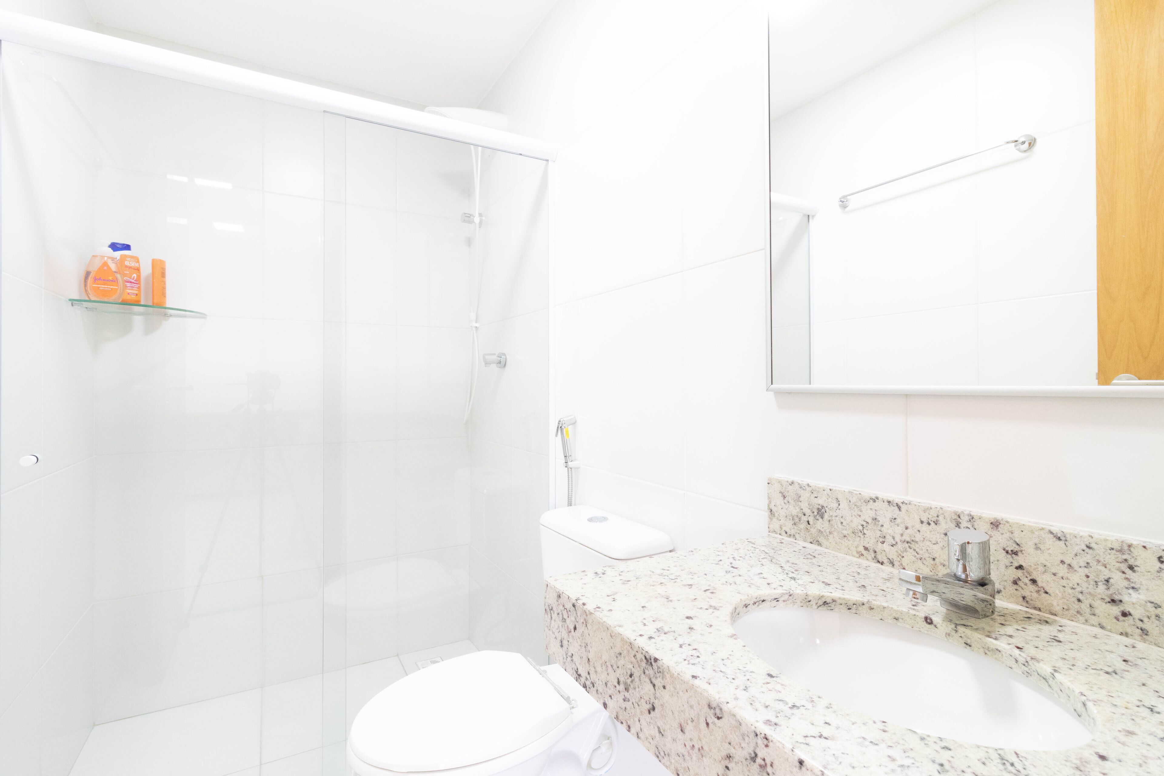 A modern bathroom with a glass shower enclosure, a white toilet, a granite countertop sink, and a mirror above the sink.