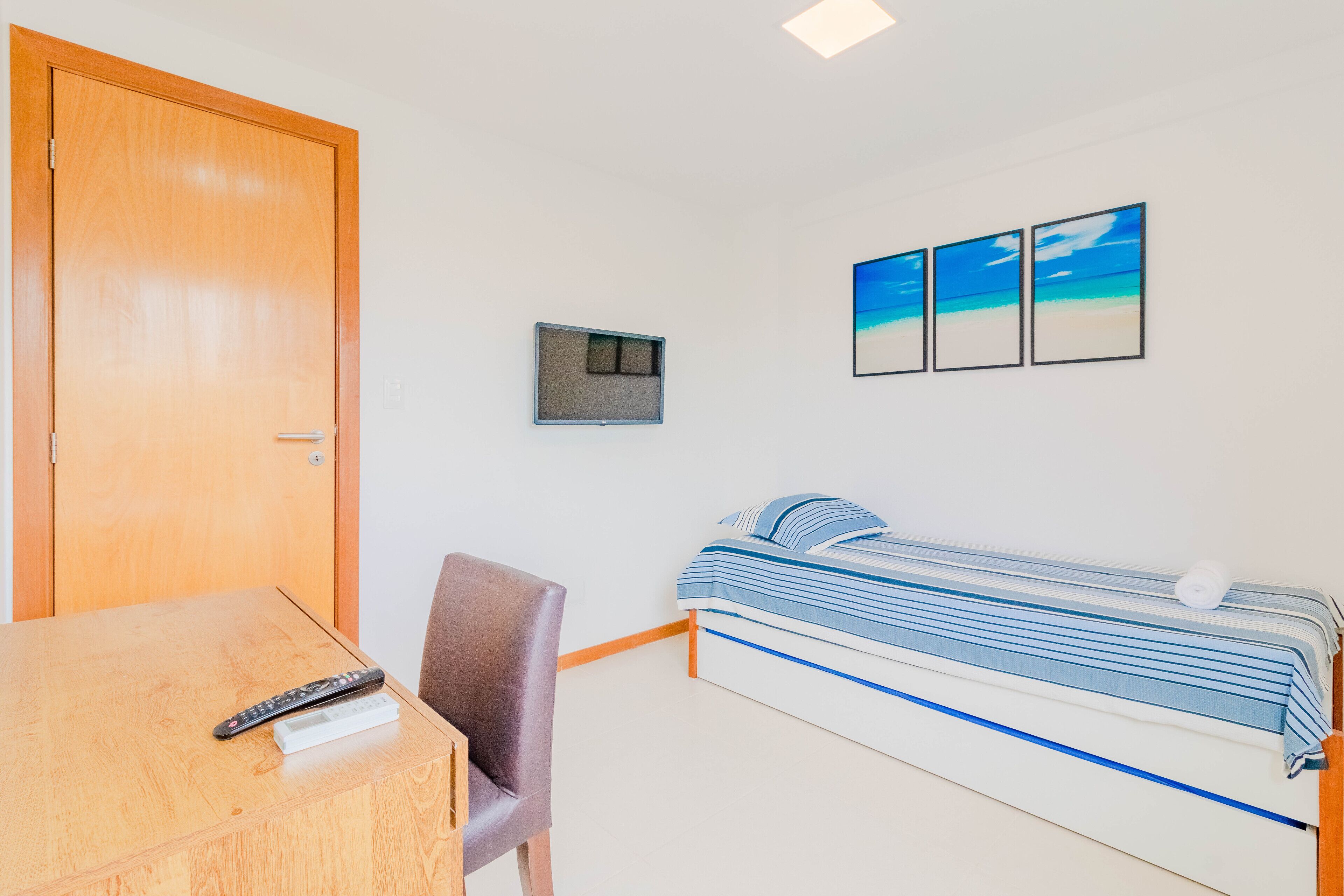 A bedroom with a bed, a desk, a chair, a TV, and a door.