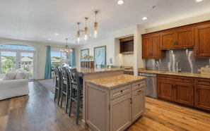 A modern kitchen with wooden cabinets, a stainless steel refrigerator, and a dining area with a white sofa and chairs. - New Rental in Seacrest Beach Resort, stunning views of Lagoon Pool, 3 bikes! (Panama City Beach)