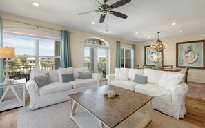 A spacious living room with white sofas, a wooden coffee table, and a view of the outdoors. - New Rental in Seacrest Beach Resort, stunning views of Lagoon Pool, 3 bikes! (Panama City Beach)