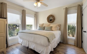 A bedroom with a bed, a ceiling fan, a wall-mounted mirror, and large windows with curtains. - New Rental in Seacrest Beach Resort, stunning views of Lagoon Pool, 3 bikes! (Panama City Beach)