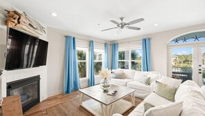 A living room with a fireplace, white sofa, blue curtains, and a ceiling fan. - New Rental in Seacrest Beach Resort, stunning views of Lagoon Pool, 3 bikes! (Panama City Beach)