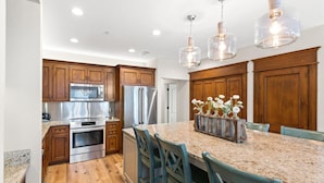 A modern kitchen with wooden cabinets, stainless steel appliances, a granite countertop, and a central island with chairs. - New Rental in Seacrest Beach Resort, stunning views of Lagoon Pool, 3 bikes! (Panama City Beach)