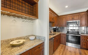 A kitchen with wooden cabinets, granite countertops, stainless steel appliances, and a wine rack with glasses.