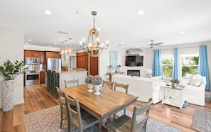 A spacious living area with a wooden dining table, white sofa, and a kitchen with wooden cabinets and stainless steel appliances.