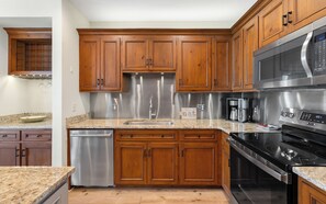 A kitchen with wooden cabinets, stainless steel appliances, a dishwasher, and granite countertops. - New Rental in Seacrest Beach Resort, stunning views of Lagoon Pool, 3 bikes! (Panama City Beach)