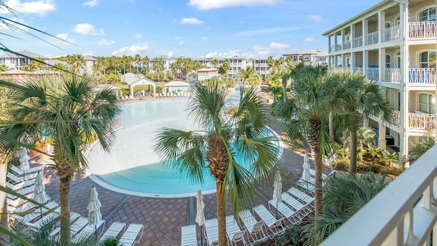 A resort pool surrounded by palm trees and lounge chairs, with a view of the hotel buildings in the background. - New Rental in Seacrest Beach Resort, stunning views of Lagoon Pool, 3 bikes! (Panama City Beach)