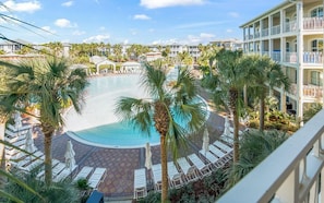 A resort pool surrounded by palm trees and lounge chairs, with a view of the hotel buildings in the background.