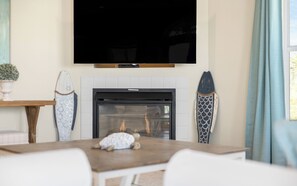 A living room with a fireplace, a flat-screen TV mounted above it, and a surfboard decoration on the wall.
