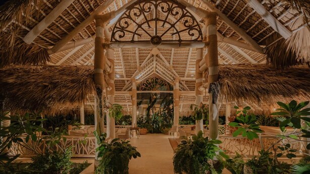 A thatched-roof structure with a central decorative metal piece, surrounded by lush greenery and seating areas. - Luxurious Fully-staffed Villa With Amazing View in Exclusive Golf Beach Resort (Punta Cana)
