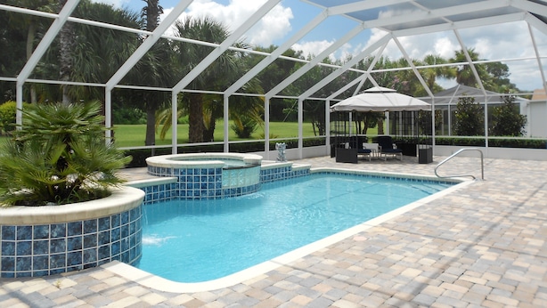 A covered swimming pool with a hot tub, lounge area, and a view of a golf course.