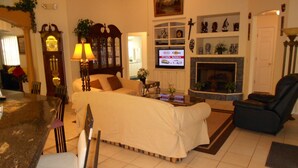 A hotel room with a bed, a desk, a chair, a television, a fireplace, and a clock.