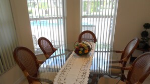 A dining table with a glass top and a white lace table runner, surrounded by wicker chairs with cushioned seats.