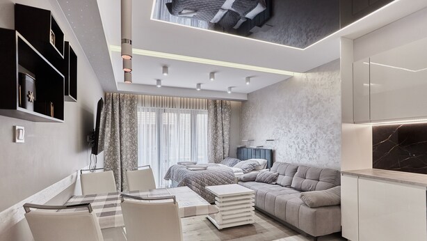 Un salon moderne comprenant un canapé, une table à manger avec des chaises, un téléviseur fixé au mur et un plafond doté d’un éclairage encastré.