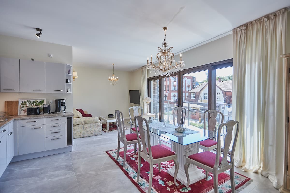 Una cocina moderna con armarios blancos y un comedor con mesa de vidrio y sillas rojas.